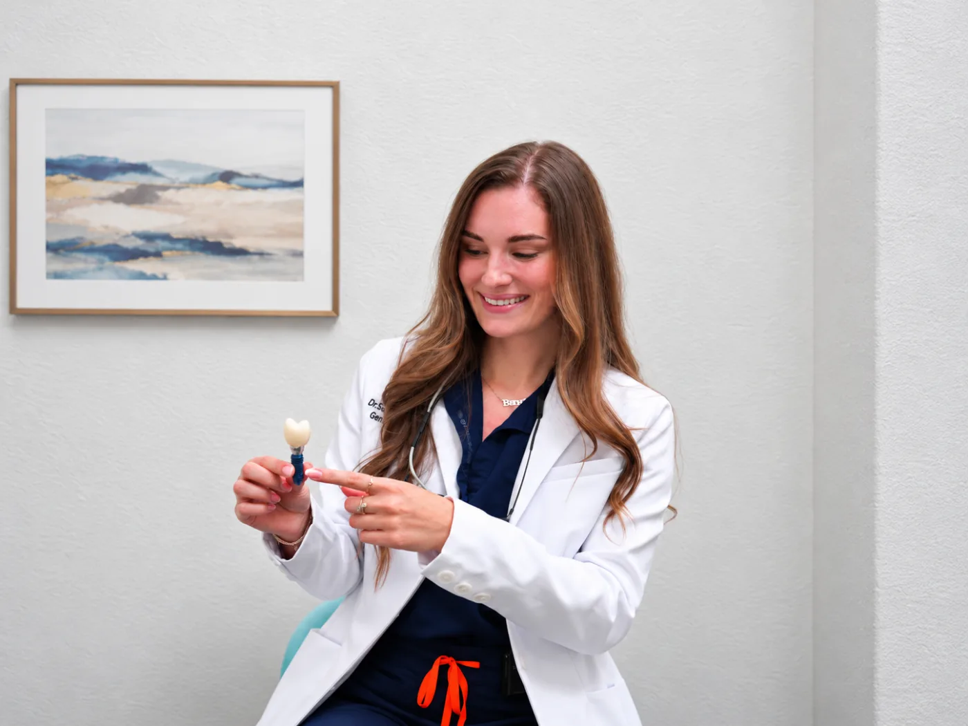 Dr. Elena Nemirovskii holding a dental implant and crown model
